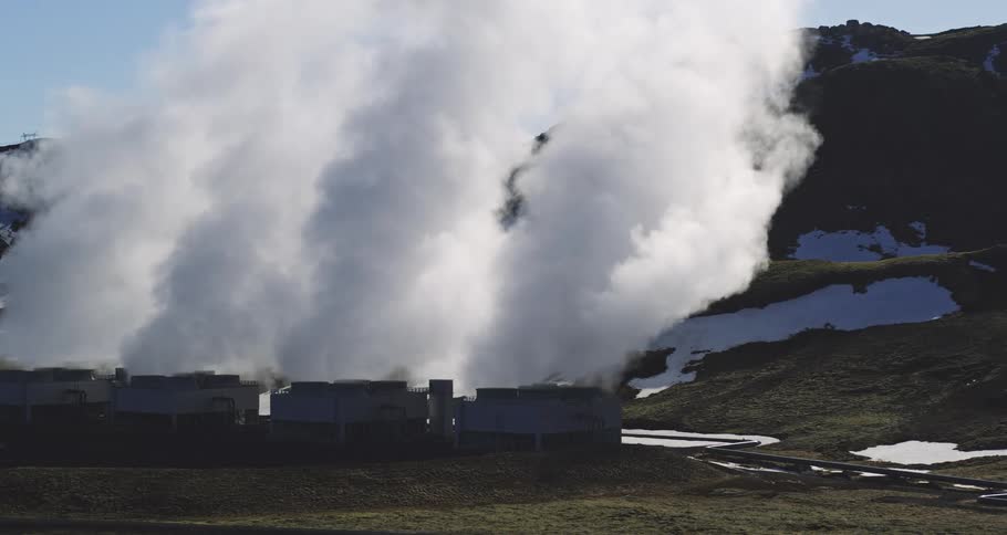 A geothermal power plant releases large plumes of steam into the atmosphere in a remote, snowy landscape