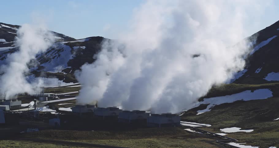 A slow zoom-out reveals a geothermal power plant releasing billows of steam in a remote, snowy mountain valley