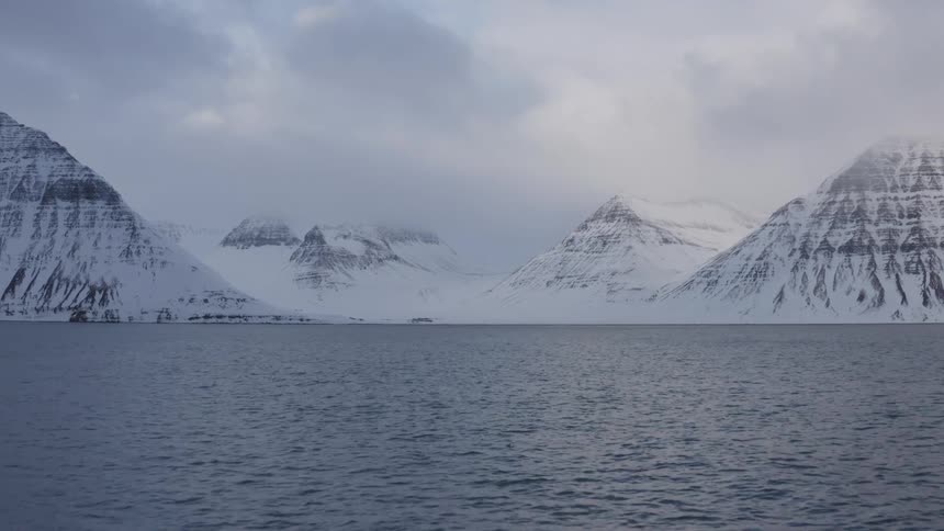 A majestic winter landscape of snow-covered mountains surrounding a calm fjord under an overcast sky