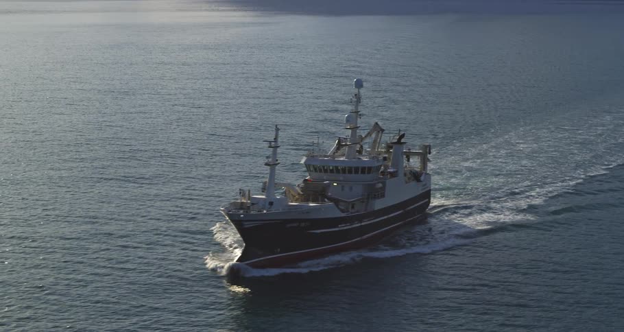 A commercial fishing vessel makes its way across the sunlit sea, leaving a wake behind it