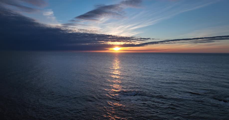 An aerial view of a glorious sunset over a calm ocean as the sun's reflection shimmers on the water's surface