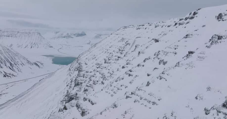 A slow rising aerial view of a majestic, snow-covered mountain overlooking a frozen valley and fjord