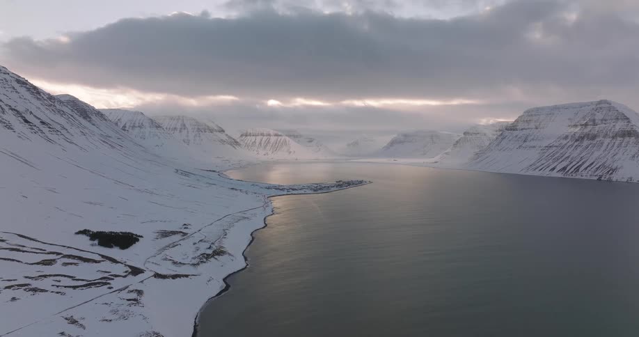 A breathtaking aerial view captures a serene fjord surrounded by majestic snow-covered mountains in Iceland during a winter sunset