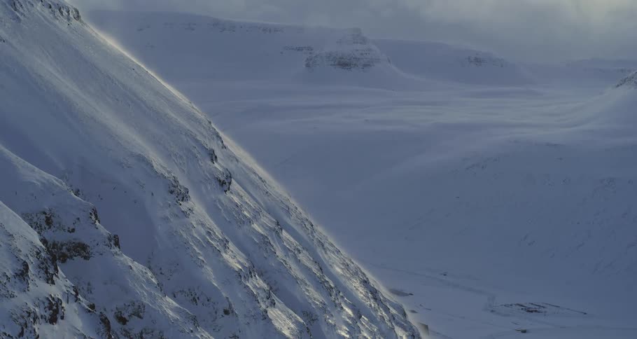 High winds blow snow across a vast and desolate winter mountain landscape