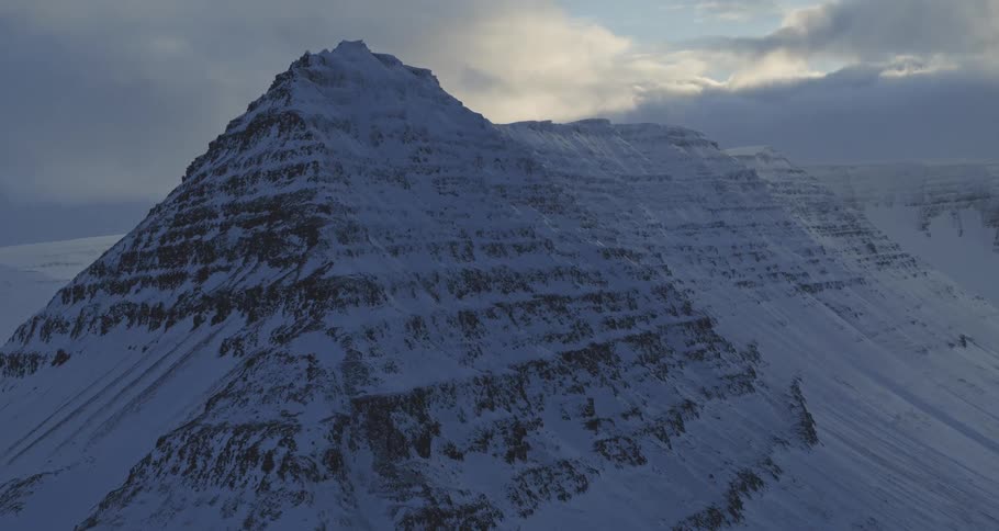 A majestic snow-covered mountain peak is silhouetted against a dramatic and moody cloudy sky