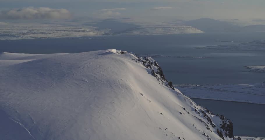 A beautiful, wide shot from a snowy mountain peak looks out over a vast and icy fjord landscape