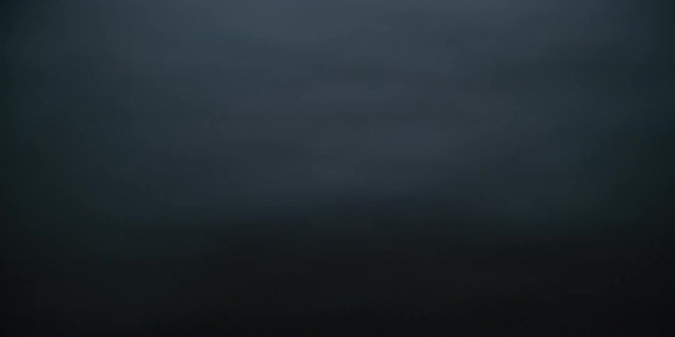 A moody close-up shot of seafoam and a dark rock on a beach before being completely submerged by a wave