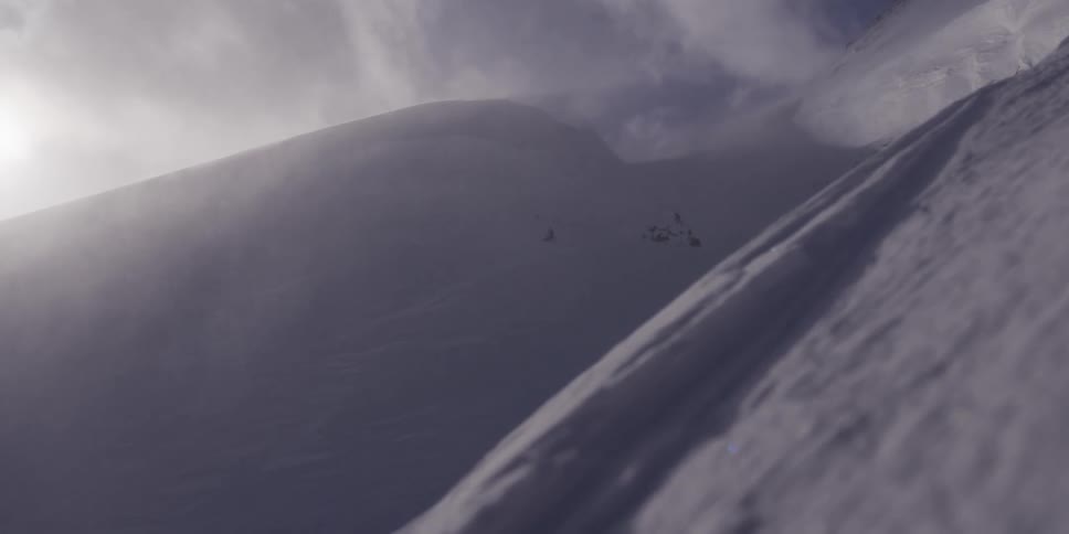A slow pan across a windswept, snow-covered mountain ridge reveals the sun breaking through a misty sky