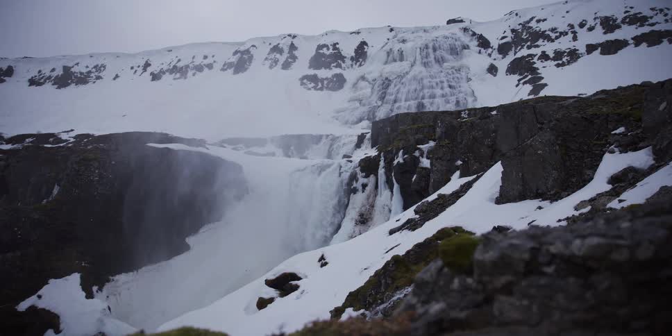 A powerful waterfall cascades through a snowy and icy canyon landscape in winter, revealed by a slow slider shot