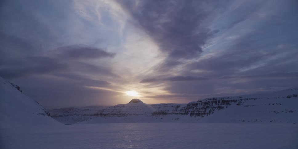 A beautiful time-lapse of a sunrise over a vast, snow-covered valley surrounded by mountains