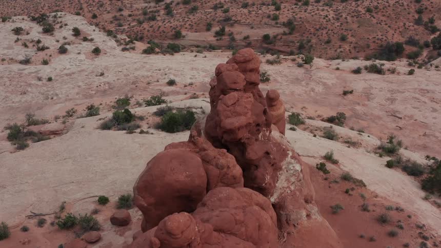 A stunning aerial view orbits a unique red rock formation in the middle of a vast desert canyon