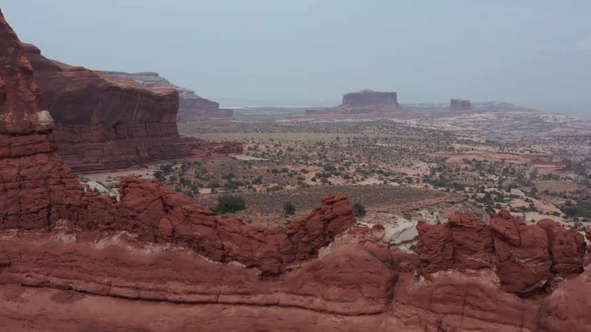 A slow aerial pan over a dramatic red rock ridge reveals the expansive desert landscape of Moab, Utah