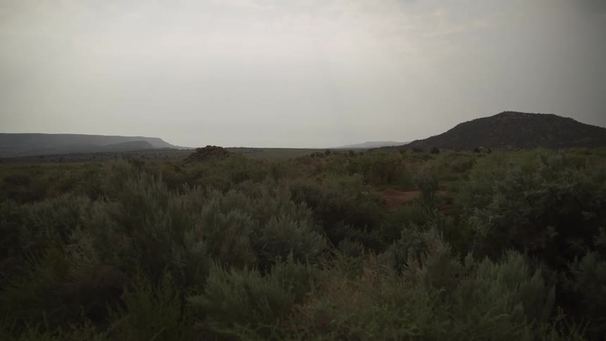 A vast, hazy desert landscape of sagebrush and mesas sits quietly under an overcast sky
