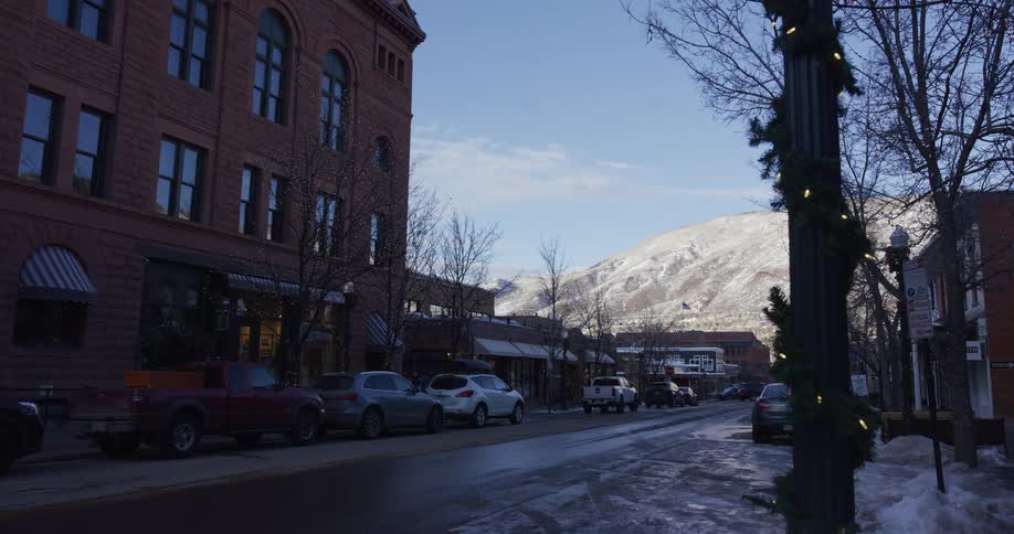A quiet winter street scene in a classic American mountain town with snow-capped mountains and holiday decorations