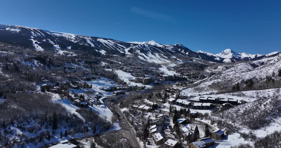 A beautiful aerial view slowly pushes in over a snowy mountain valley revealing a popular ski resort on a bright sunny day