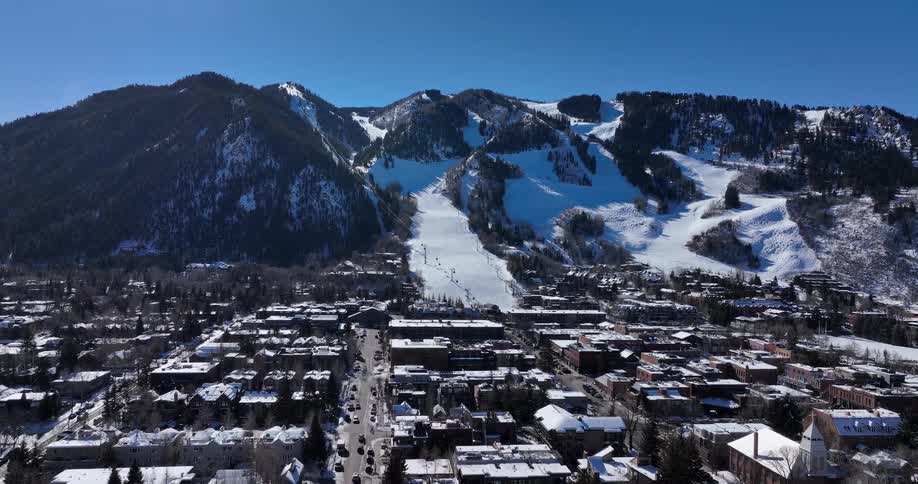 Wide aerial view of a bustling ski resort town nestled at the base of a snow-covered mountain on a bright and sunny winter day