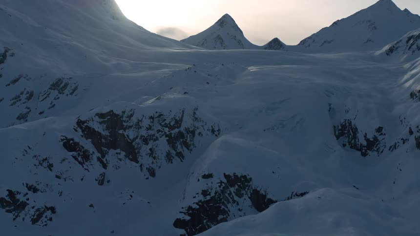 An epic aerial shot reveals a vast, snow-covered mountain valley with towering peaks at dawn