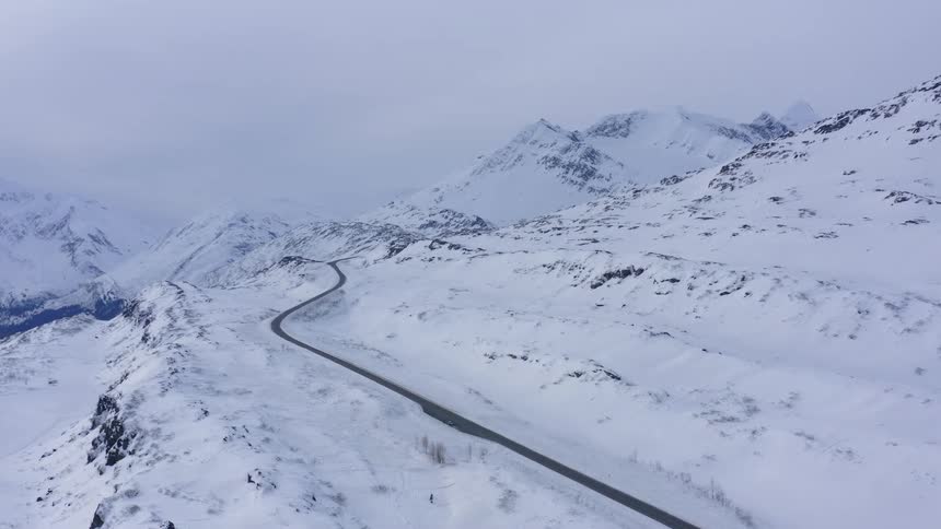 A desolate road winds through a vast and empty snow-covered mountain pass