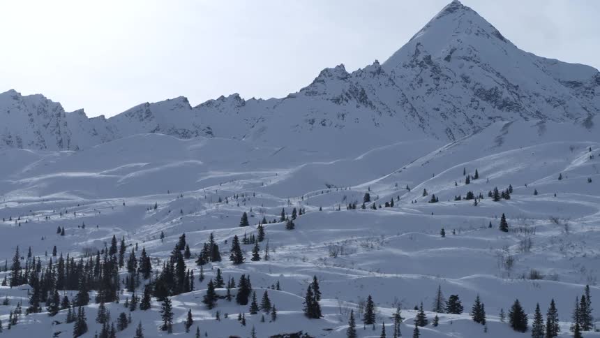 An aerial view slowly pulls back over an expansive winter wonderland with snow-covered hills and a majestic mountain peak