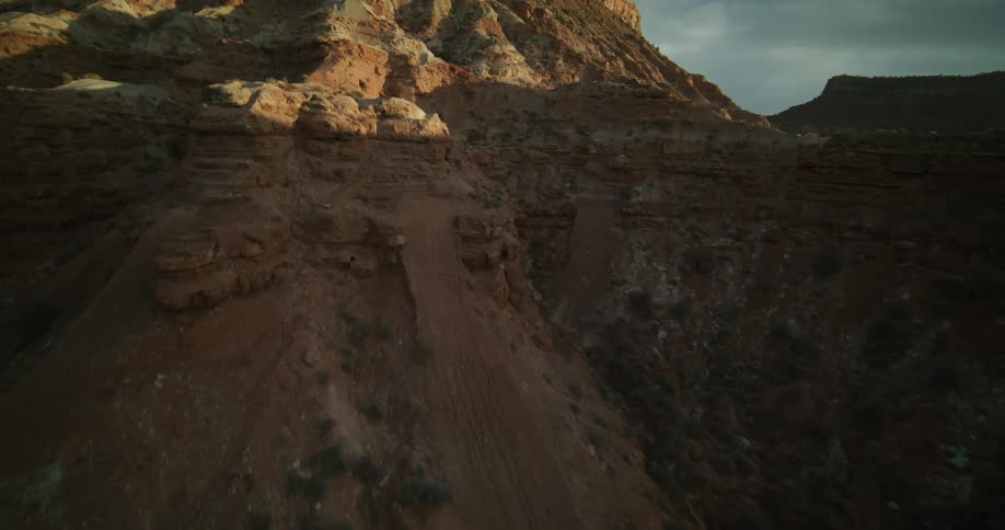An aerial shot slowly flies along a majestic red rock canyon wall, illuminated by the warm light of sunrise