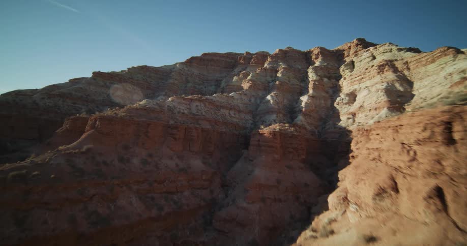 A thrilling, low-altitude drone flight speeds past the layered red rock formations of a desert canyon under a clear blue sky
