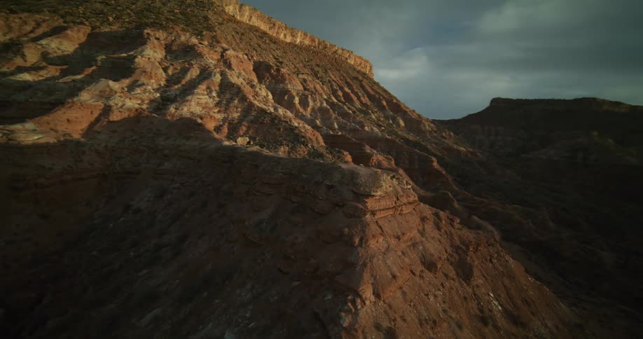 A majestic aerial view orbits a sun-kissed red rock mountain in a vast desert landscape during a dramatic golden hour