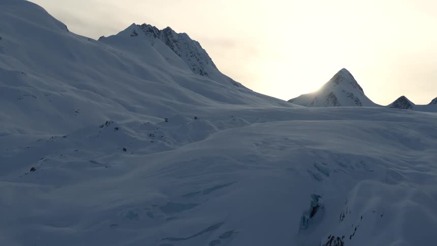 The morning sun crests over the peak of a vast, frozen mountain landscape covered in deep snow