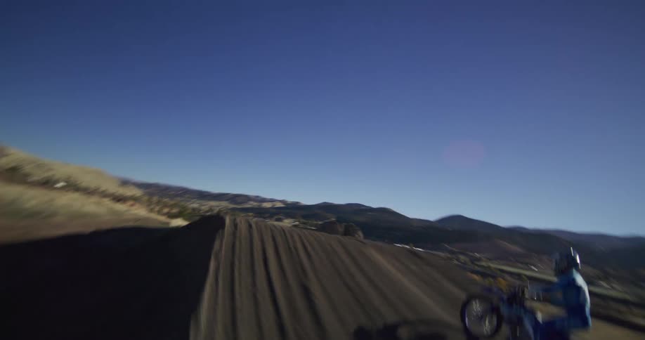 A motocross rider wearing blue gear launches off a large dirt jump in dramatic slow motion on a sunny day