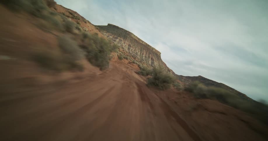 A thrilling first-person-view journey down a winding dirt road surrounded by red rock mesas and desert brush