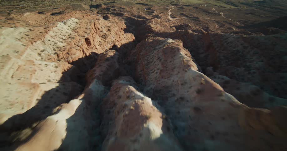 An exhilarating aerial flight begins with a top-down view before tilting up to soar over a rugged red rock canyon landscape in the desert