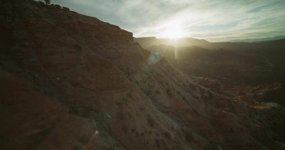 A stunning aerial view flies over a rugged mountain ridge in a vast desert canyon landscape at golden hour