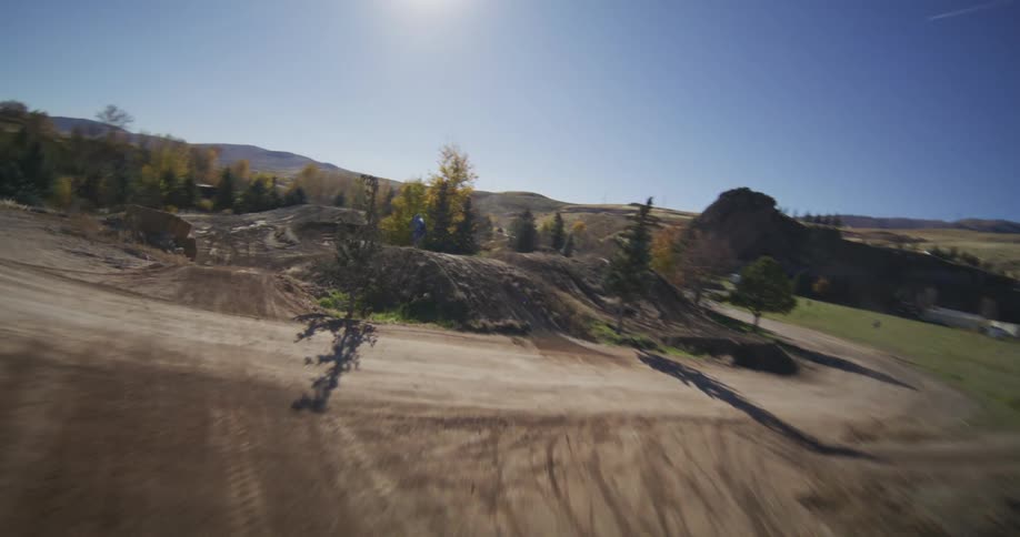 High-speed FPV drone chases a motocross biker launching off jumps and navigating a challenging dirt track