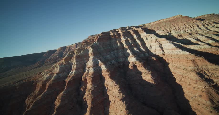 Aerial footage reveals the majestic, layered rock formations of a vast desert mountain range under a clear blue sky