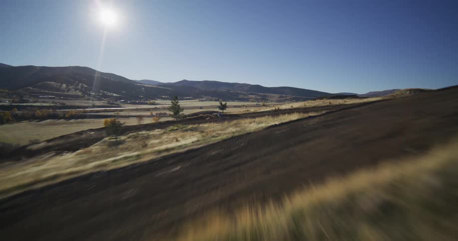 Dynamic first-person drone footage flies at high speed over a winding dirt motocross track in a sunny rural valley