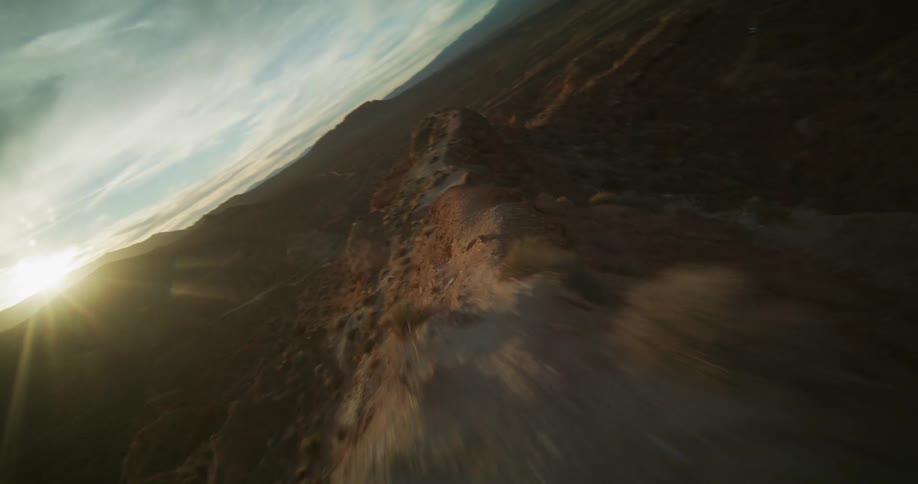 A cinematic FPV drone flight soars along a rugged desert ridgeline at sunset, revealing the vast and beautiful canyon landscape
