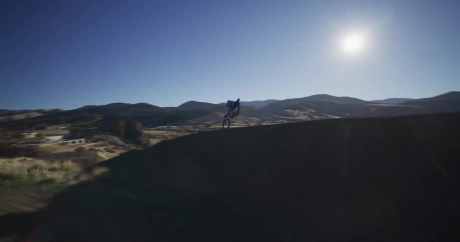 Thrilling FPV drone footage follows a motocross rider down a dirt track, capturing a massive jump in dramatic slow motion