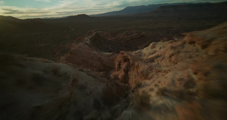 A breathtaking first-person view drone flight soars along a steep, rocky desert ridge at sunset, revealing the vast canyon below