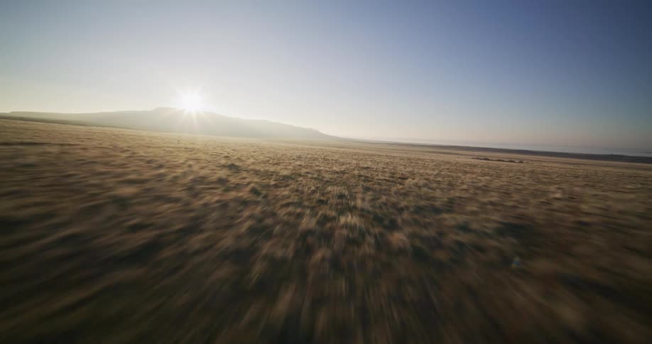 Soaring aerial view over an empty desert road and vast grasslands at sunrise