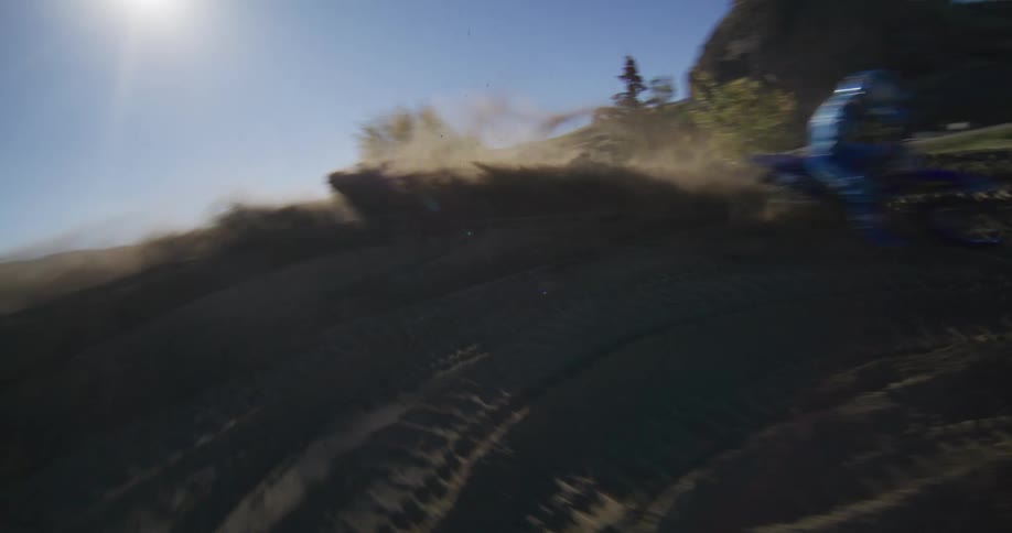 Motocross rider expertly rounds a dirt berm, sending a massive plume of dust into the air in dramatic slow motion