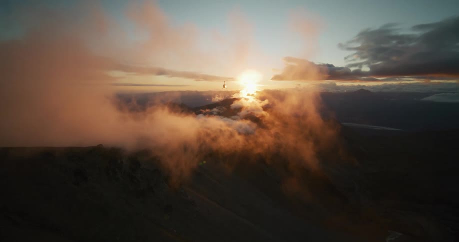A stunning aerial view shows a helicopter flying towards the golden sunset over a vast and cloudy mountain range
