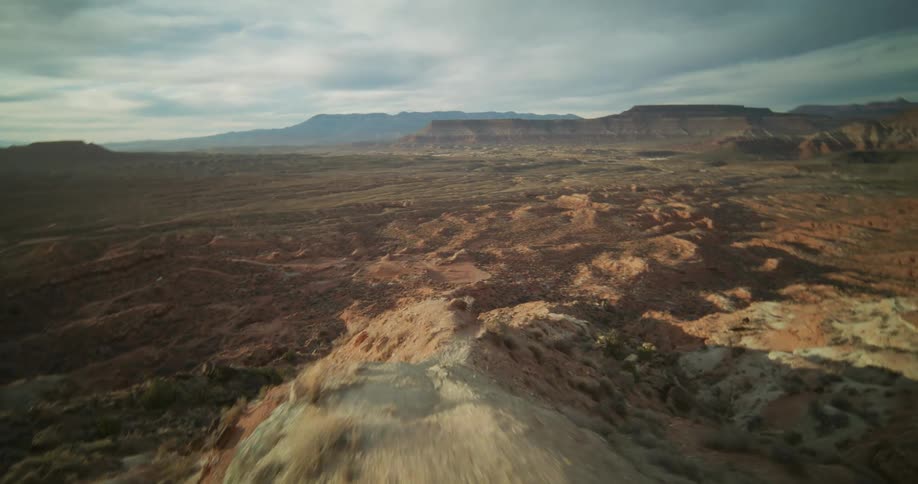 An FPV drone perspective of a thrilling, high-speed flight along a rugged desert ridgeline overlooking a vast red rock canyon