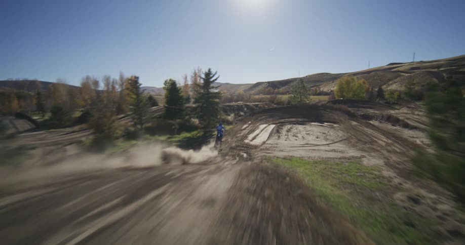 Slow-motion follow shot of a motocross rider catching air off a big jump and speeding around a dusty turn on a sunny day