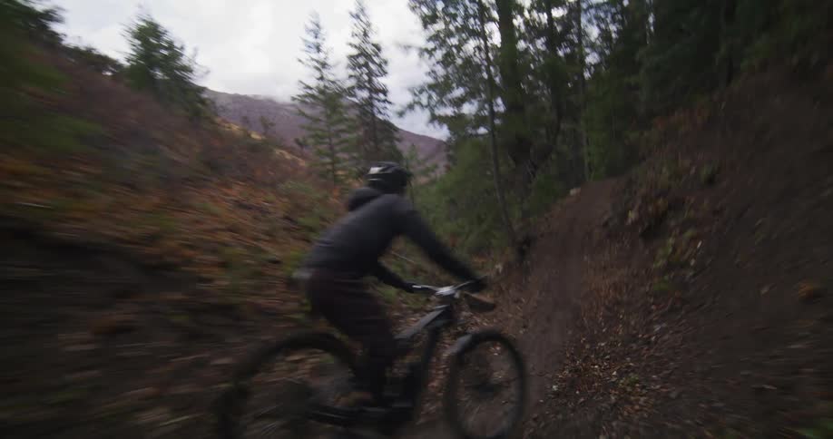 A mountain biker speeds down a dark, winding forest trail in slow motion