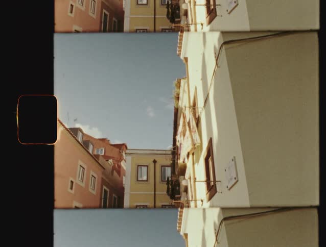 Vintage film strip style footage of a sunlit alley between colorful European apartment buildings