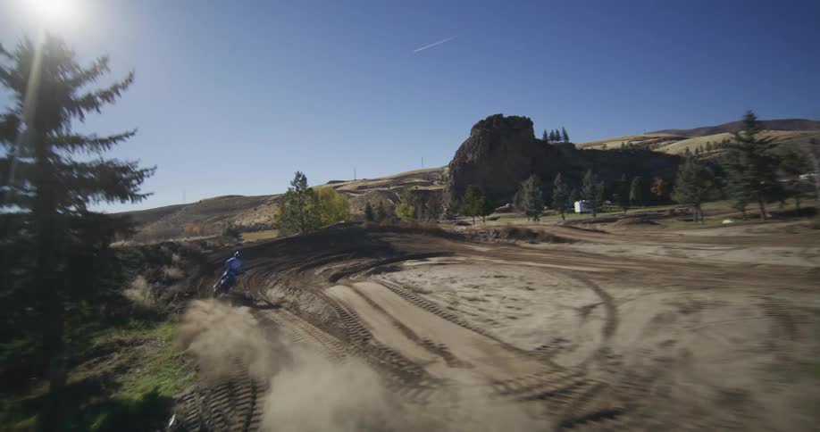 Slow motion shot of a motocross rider jumping and then turning sharply on a dusty dirt track under a clear blue sky