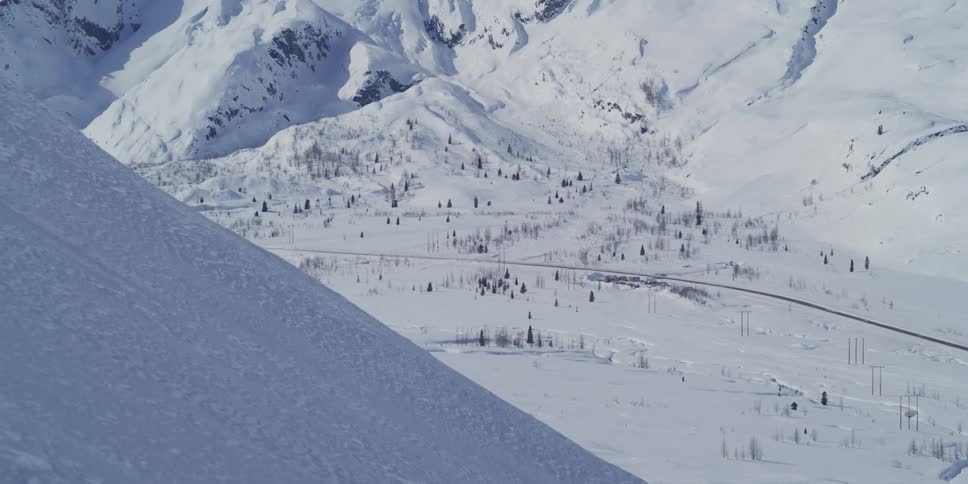 A slow zoom out from a snowy mountain side reveals a vast, epic winter landscape and valley below