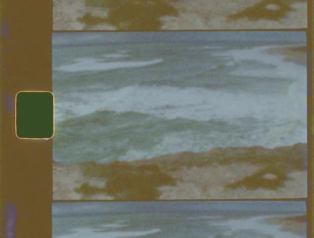 Vintage 8mm film pans across a scenic, rugged coastline with ocean waves gently rolling onto the shore