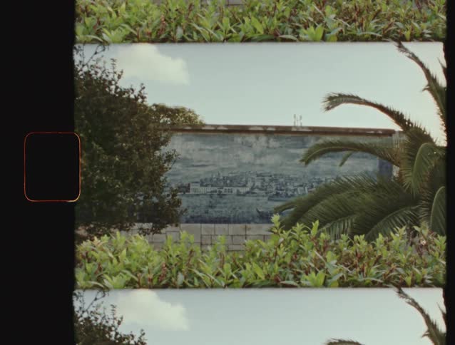 Vintage filmstrip view of a traditional Portuguese azulejo tile mural depicting a cityscape, seen through lush green garden foliage