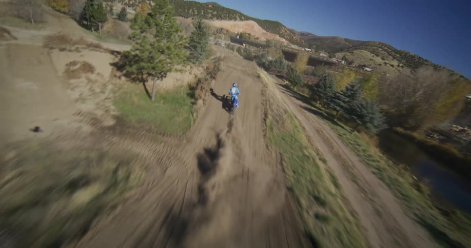 An immersive FPV drone follows closely behind a motocross rider kicking up dust and catching air on a dirt track