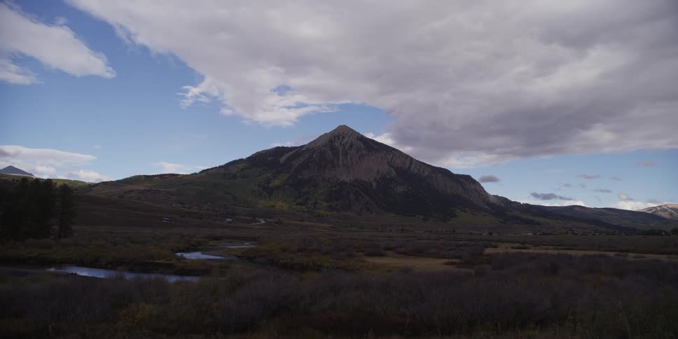 A dramatic timelapse of clouds and shadows moving over a mountain landscape, as a storm rolls in and a rainbow appears
